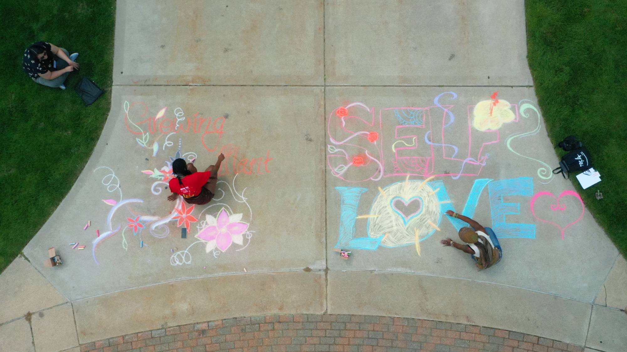 from above, students are seen drawing with chalk on the sidewalk. writing messages of self-care and love